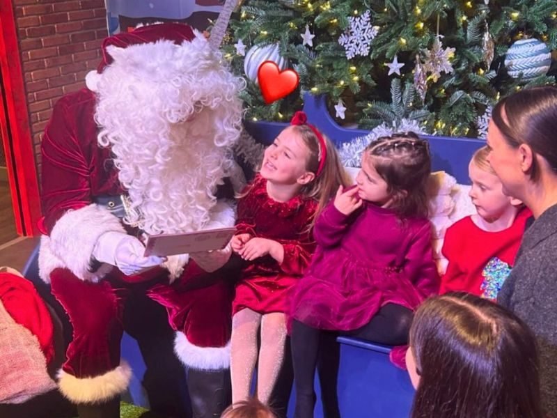Children sit with father christmas as he reads out their letters to santa